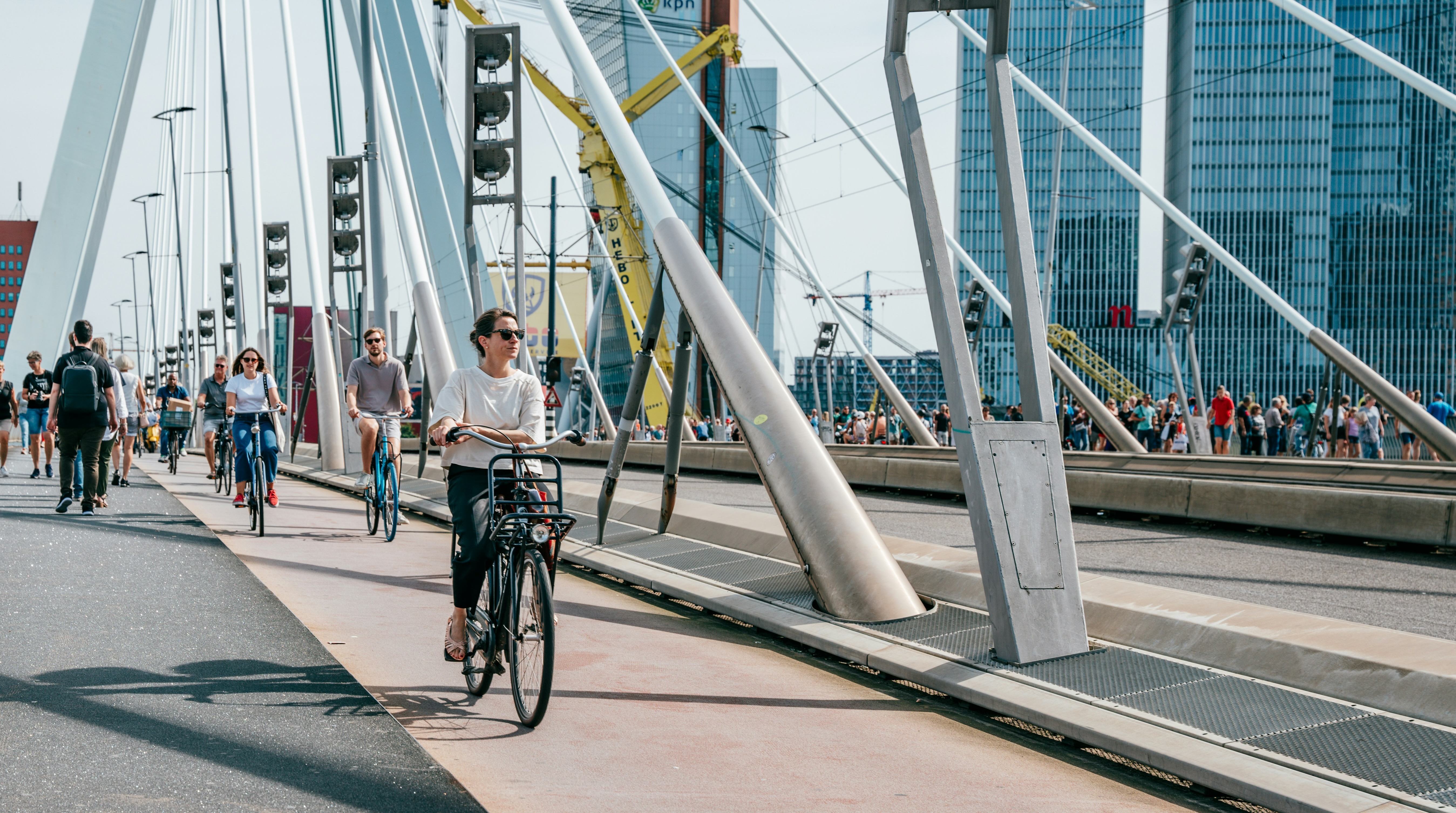 Cyclists and pedestrians crossing a bridge in a city with tall buildings behind them.